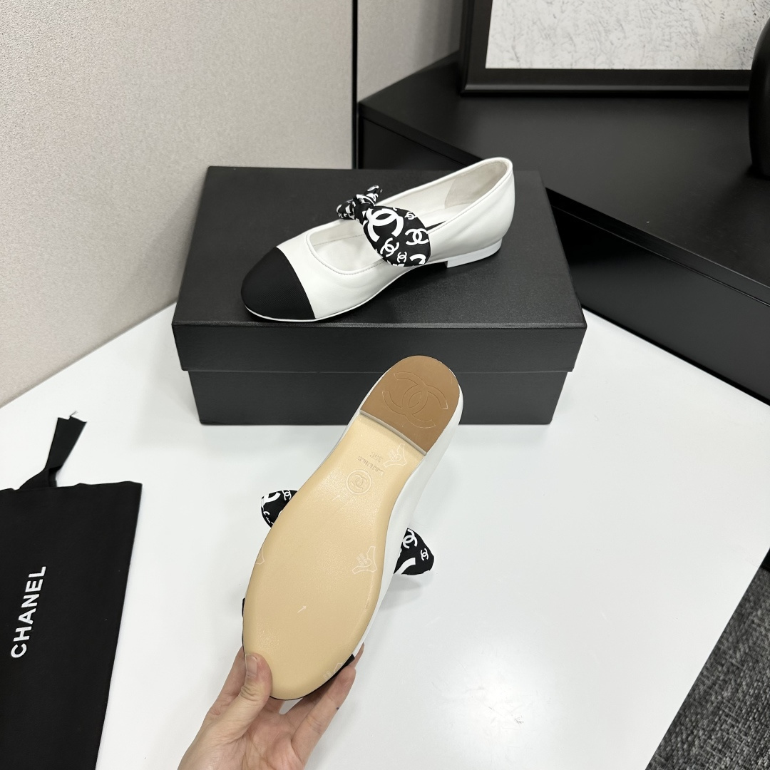 Elegant white leather ballet flats with a black cap toe and a printed CC logo bow detail resting on a black shoe box. - Hình 4