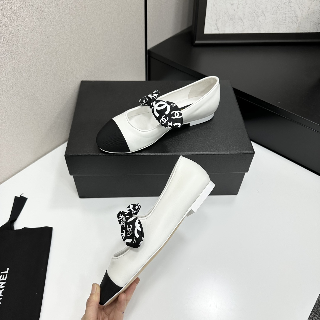 Elegant white leather ballet flats with a black cap toe and a printed CC logo bow detail resting on a black shoe box. - Hình 3