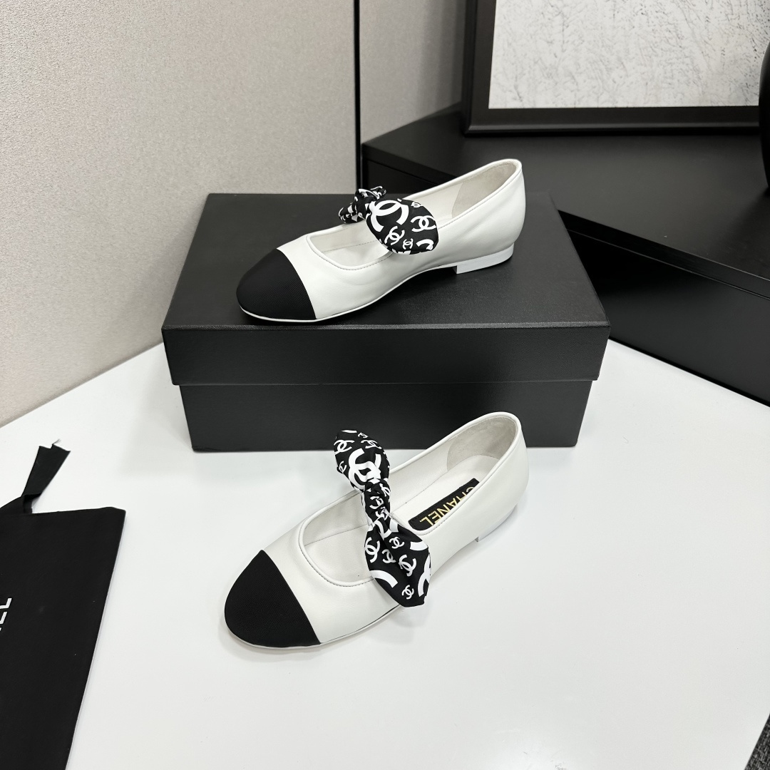Elegant white leather ballet flats with a black cap toe and a printed CC logo bow detail resting on a black shoe box. - Hình 2