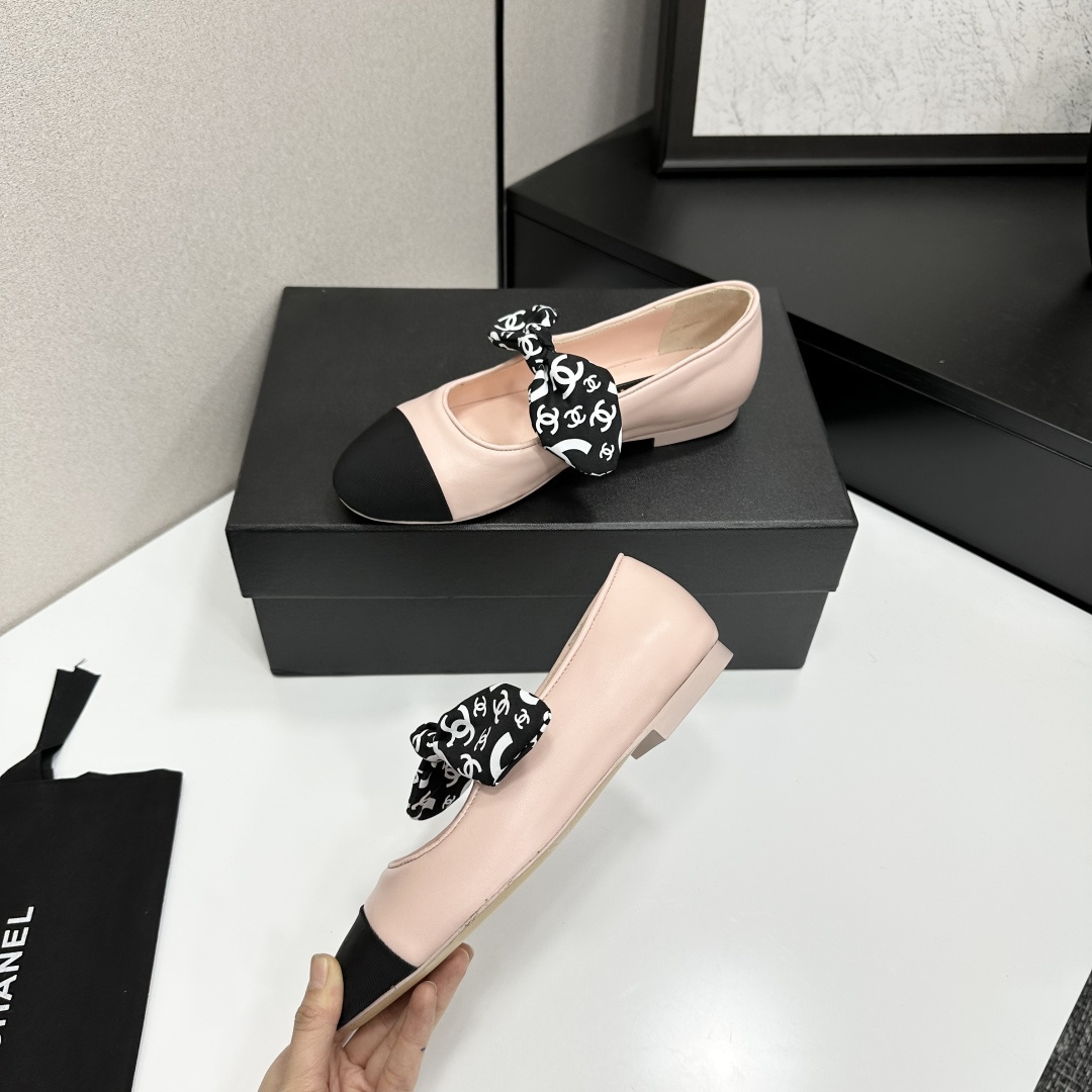 Pair of light pink luxury ballerina flats with black toe caps and patterned bows on a black display box - Hình 3