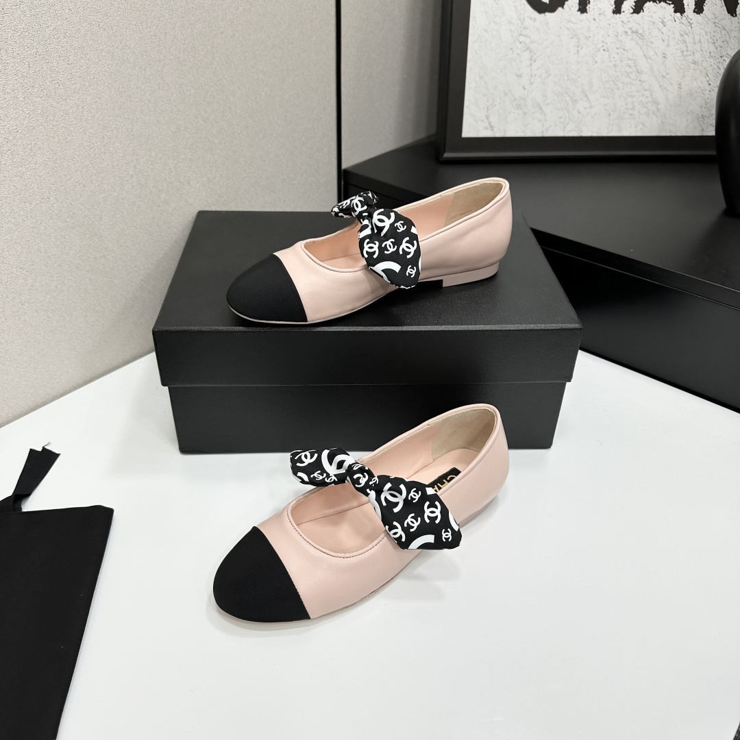 Pair of light pink luxury ballerina flats with black toe caps and patterned bows on a black display box - Hình 2