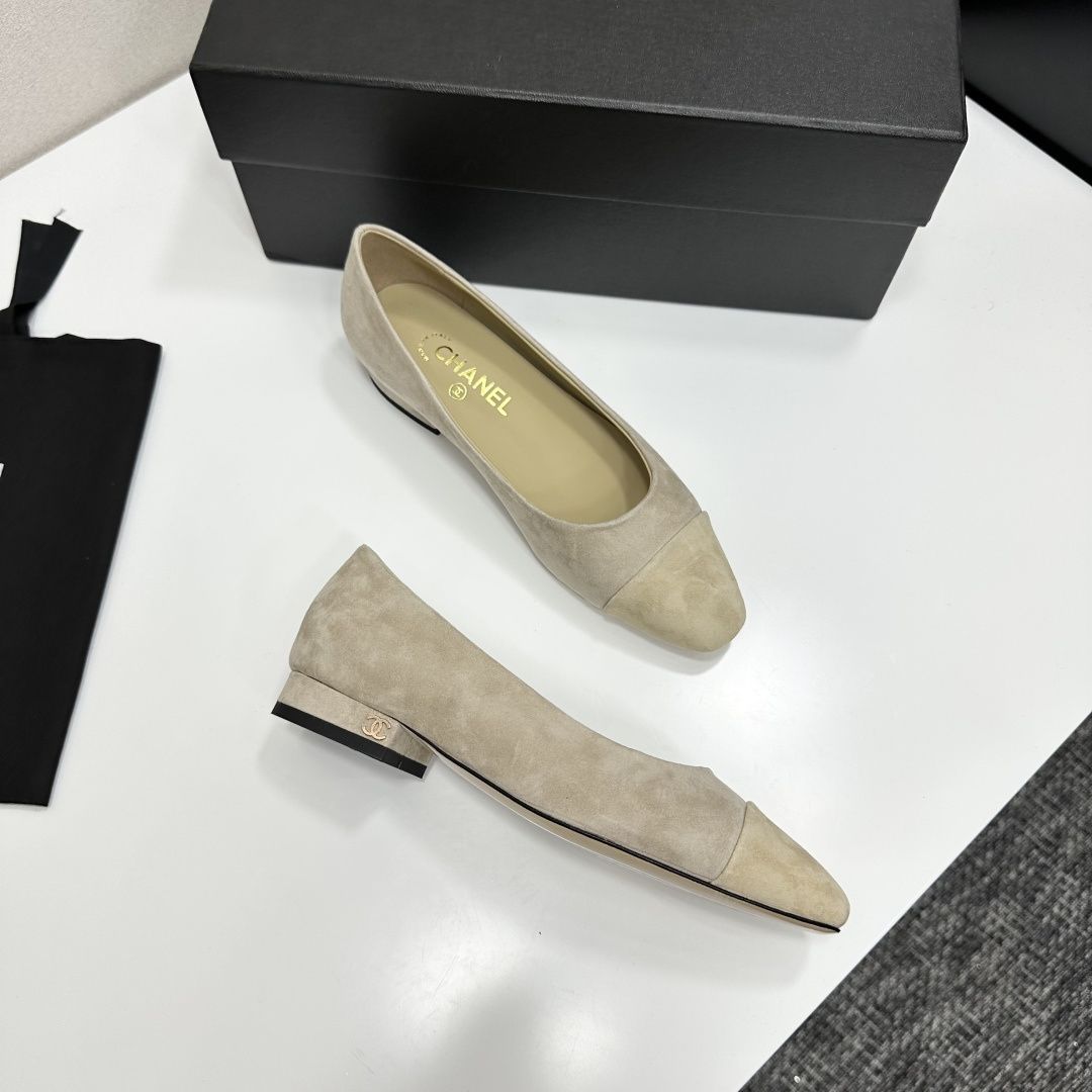 A pair of Chanel beige suede cap-toe pumps with a small block heel featuring a gold CC logo, displayed on a black box. - Hình 9