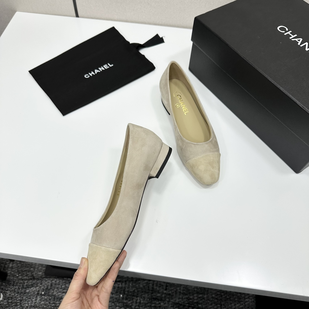 A pair of Chanel beige suede cap-toe pumps with a small block heel featuring a gold CC logo, displayed on a black box. - Hình 7
