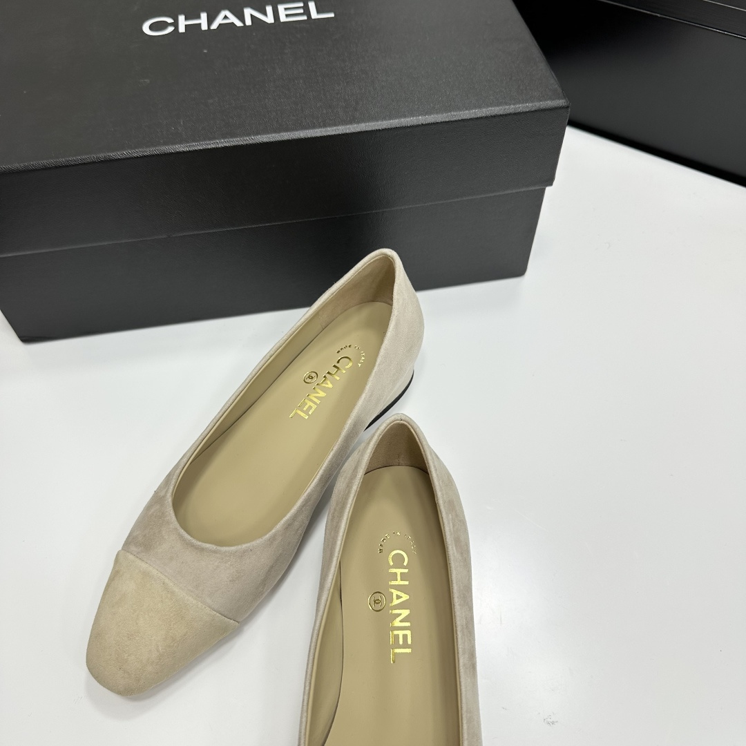 A pair of Chanel beige suede cap-toe pumps with a small block heel featuring a gold CC logo, displayed on a black box. - Hình 6