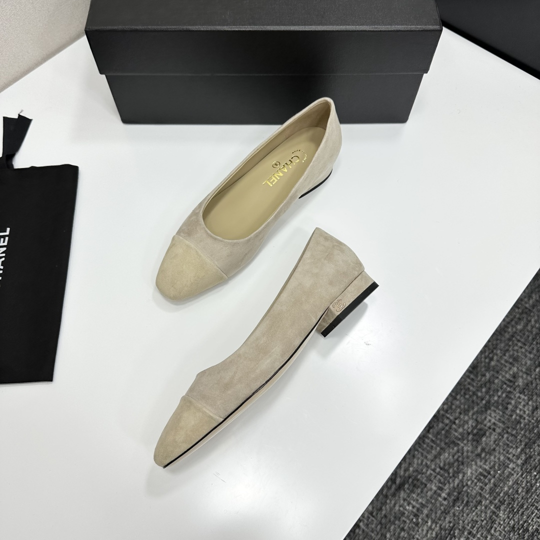 A pair of Chanel beige suede cap-toe pumps with a small block heel featuring a gold CC logo, displayed on a black box. - Hình 5