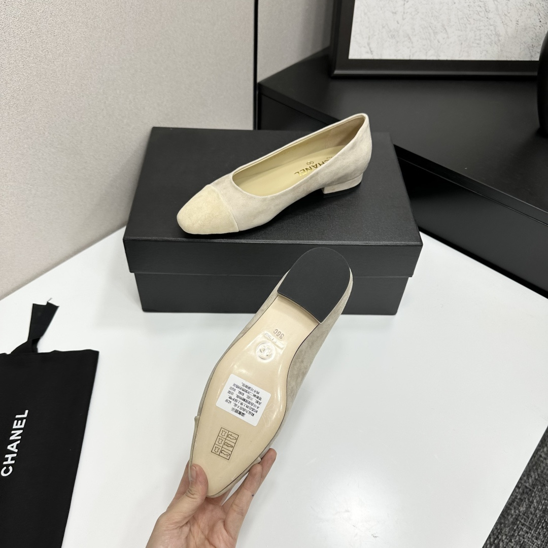 A pair of Chanel beige suede cap-toe pumps with a small block heel featuring a gold CC logo, displayed on a black box. - Hình 4