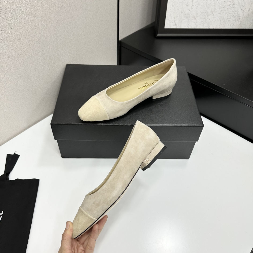A pair of Chanel beige suede cap-toe pumps with a small block heel featuring a gold CC logo, displayed on a black box. - Hình 3