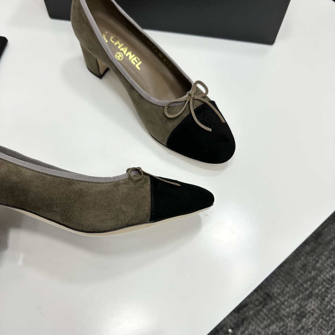 A pair of Chanel two-tone khaki and black suede pumps with a block heel and bow detail displayed on a black box. - Hình 9