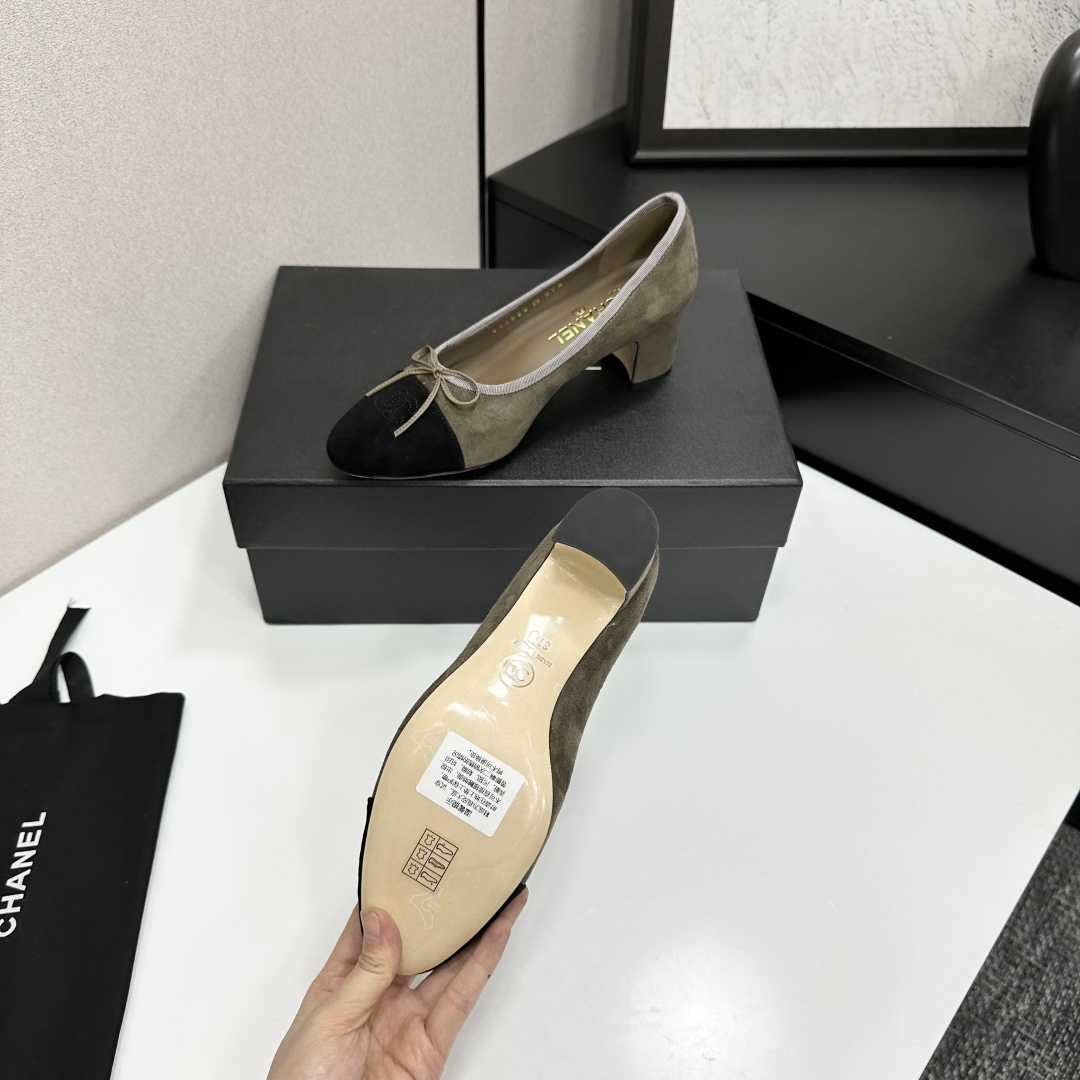 A pair of Chanel two-tone khaki and black suede pumps with a block heel and bow detail displayed on a black box. - Hình 4