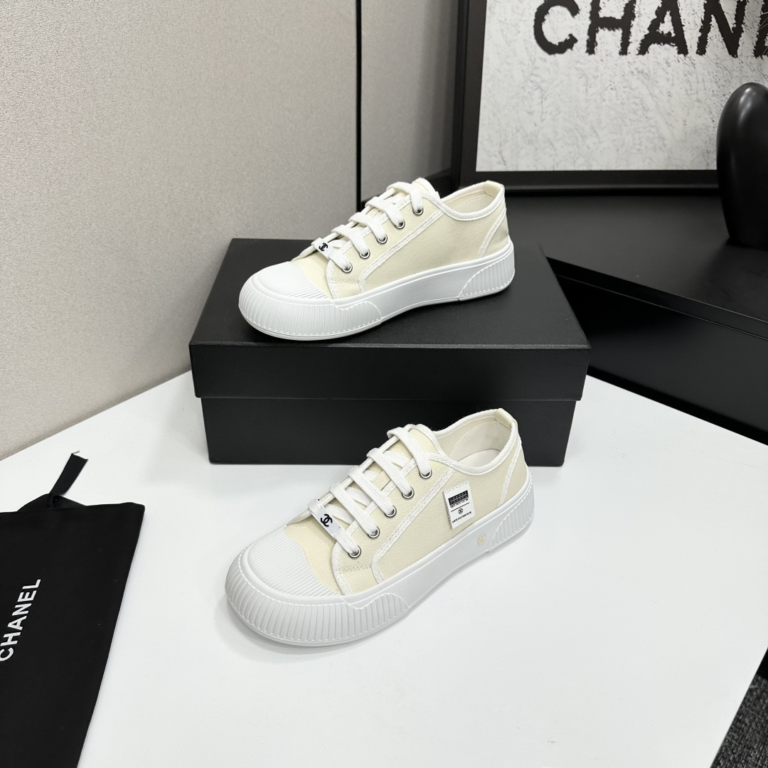 Pair of premium cream canvas low-top sneakers with a chunky white rubber sole and designer logo details displayed on a black box. - Hình 2