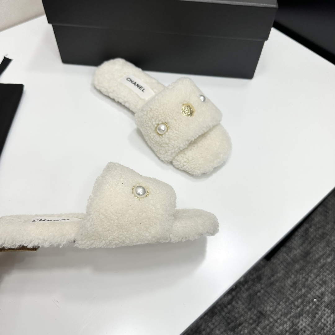A pair of white Chanel shearling slippers featuring pearl and gold CC logo embellishments sitting on a black designer box. - Hình 8