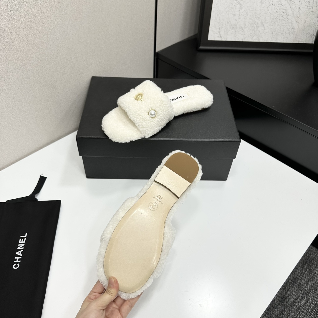 A pair of white Chanel shearling slippers featuring pearl and gold CC logo embellishments sitting on a black designer box. - Hình 4