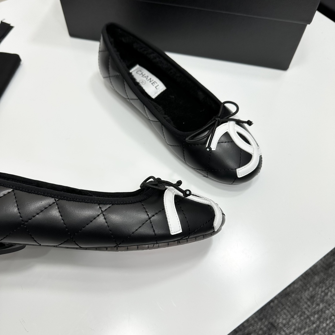 A pair of black quilted Chanel ballet flats with white CC logo on the toe and shearling lining, resting on a black box. - Hình 9