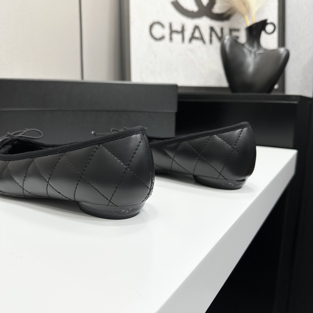 A pair of black quilted Chanel ballet flats with white CC logo on the toe and shearling lining, resting on a black box. - Hình 7