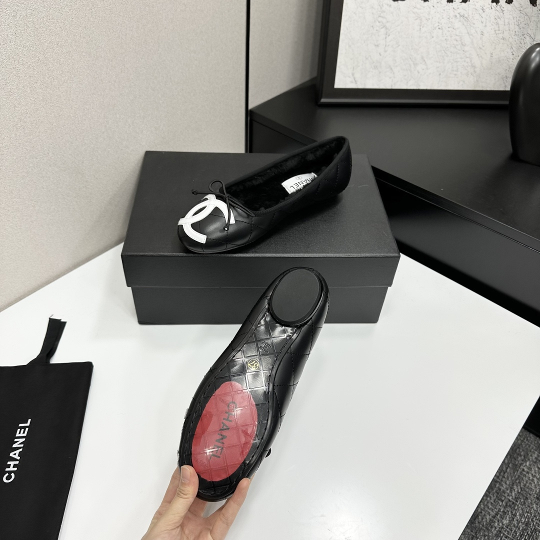 A pair of black quilted Chanel ballet flats with white CC logo on the toe and shearling lining, resting on a black box. - Hình 4