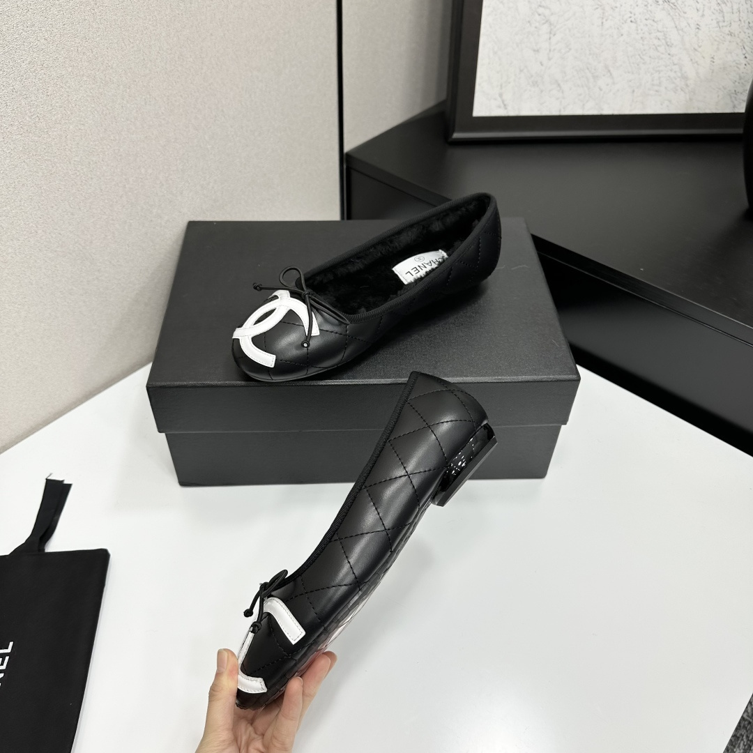 A pair of black quilted Chanel ballet flats with white CC logo on the toe and shearling lining, resting on a black box. - Hình 3