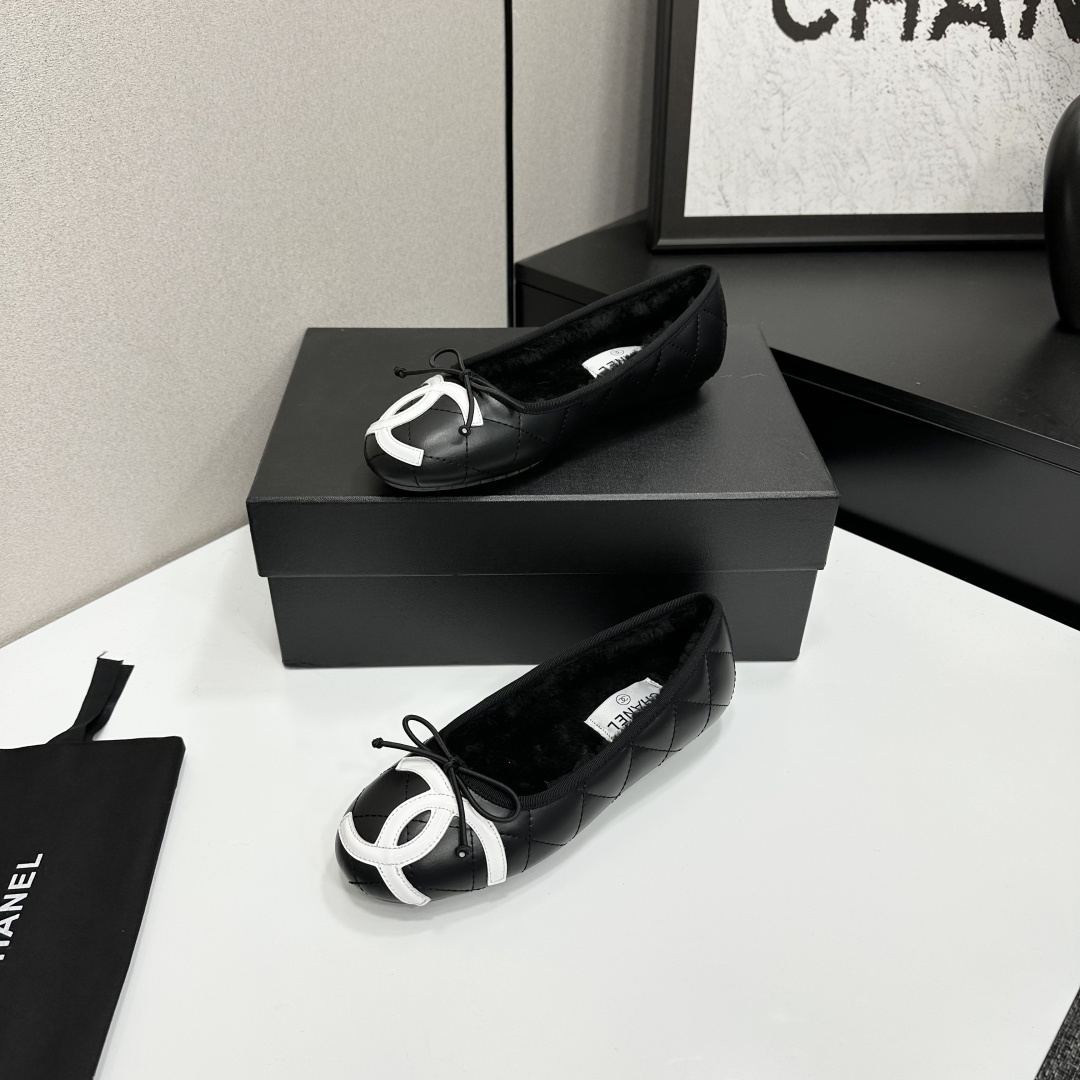 A pair of black quilted Chanel ballet flats with white CC logo on the toe and shearling lining, resting on a black box. - Hình 2