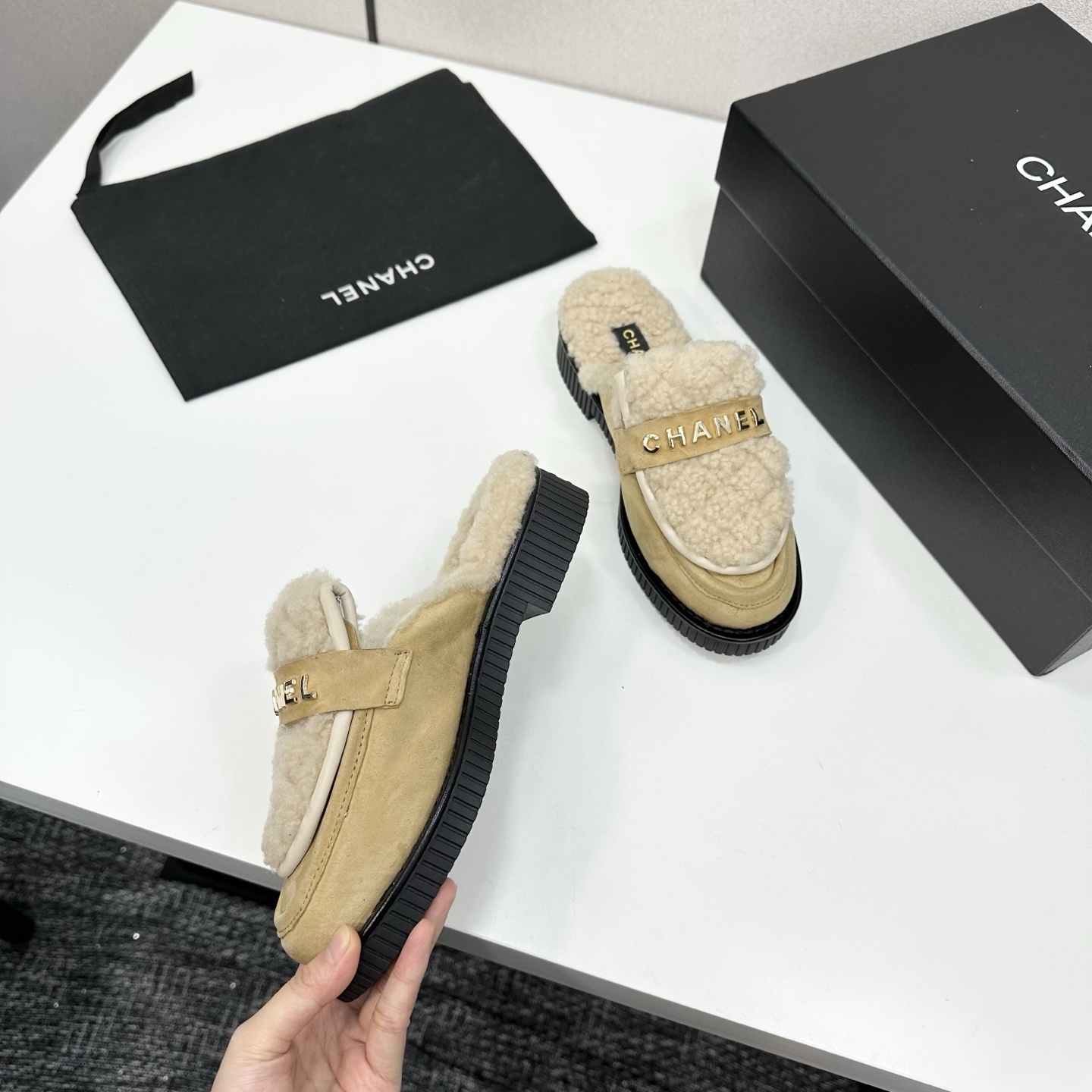 Chanel beige suede mules with cream shearling lining and gold logo strap displayed on a black box. - Hình 8