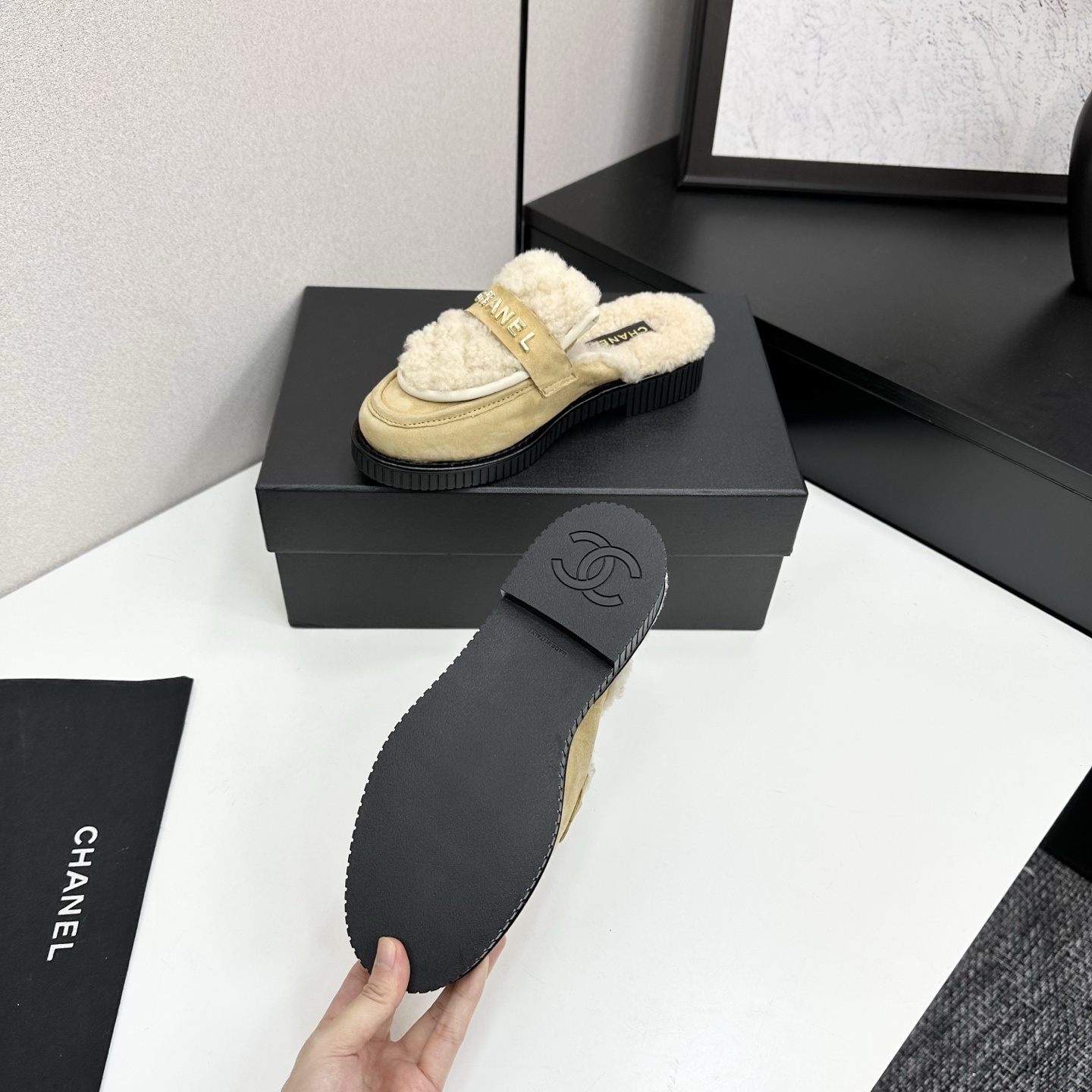 Chanel beige suede mules with cream shearling lining and gold logo strap displayed on a black box. - Hình 4