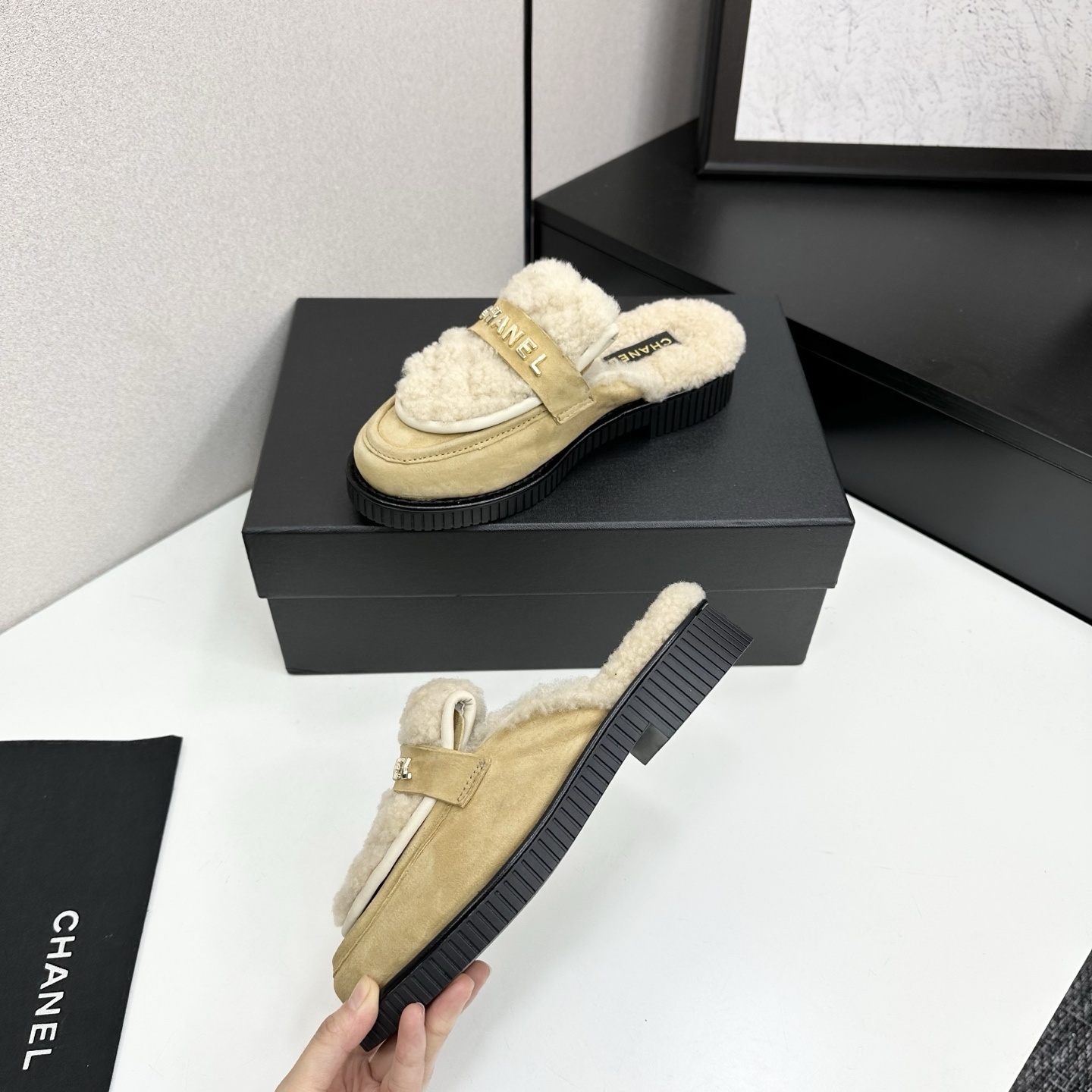Chanel beige suede mules with cream shearling lining and gold logo strap displayed on a black box. - Hình 3