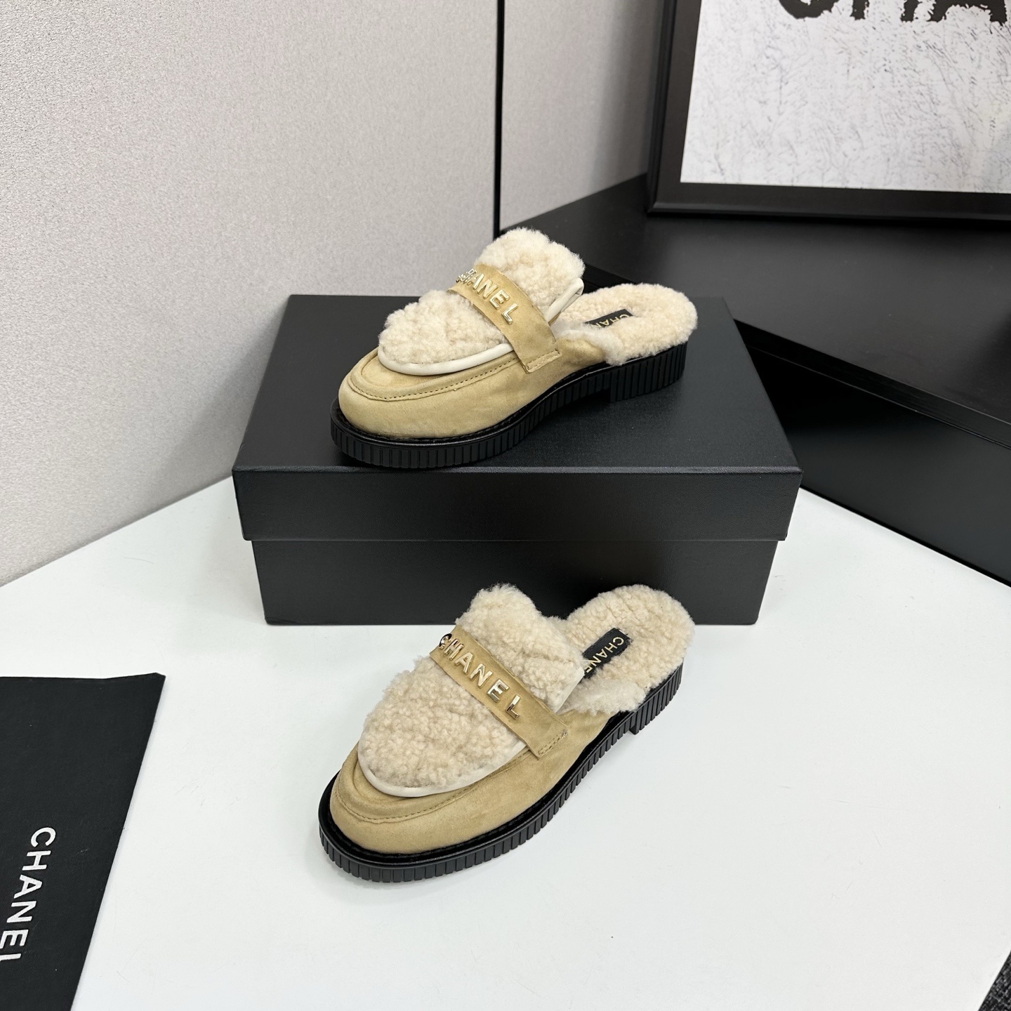 Chanel beige suede mules with cream shearling lining and gold logo strap displayed on a black box. - Hình 2