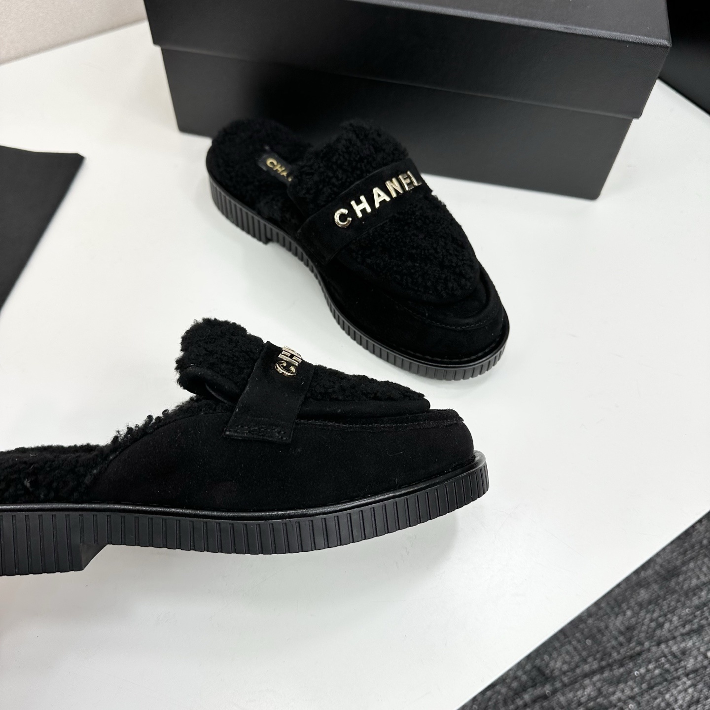 A pair of luxury Chanel black suede mules with fuzzy shearling lining and gold-tone logo hardware on a black platform sole. - Hình 9