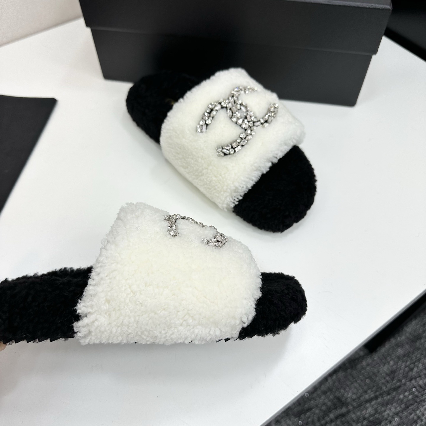 Pair of black and white fluffy shearling slides with a crystal-embellished interlocking logo sitting on a black box - Hình 9