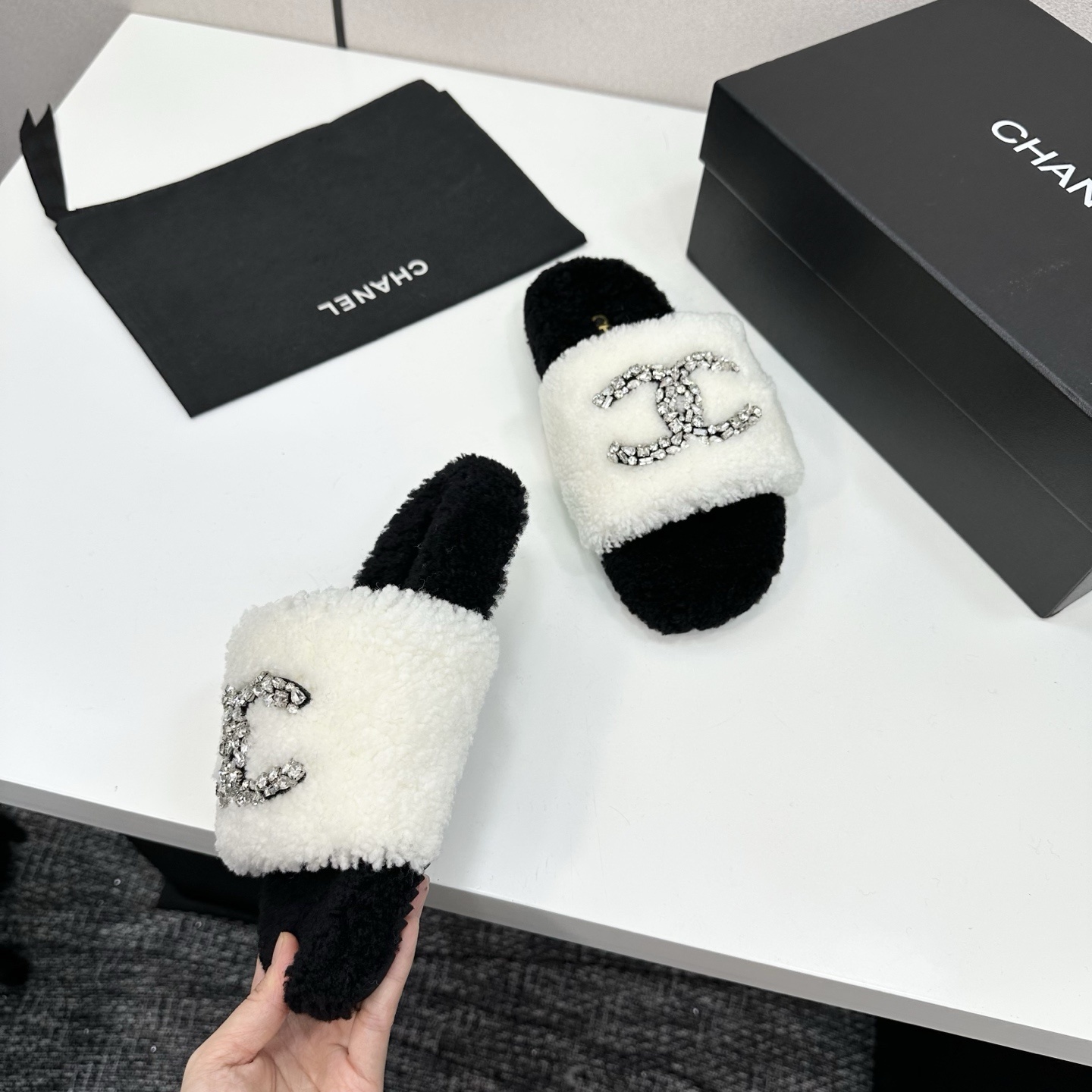 Pair of black and white fluffy shearling slides with a crystal-embellished interlocking logo sitting on a black box - Hình 8