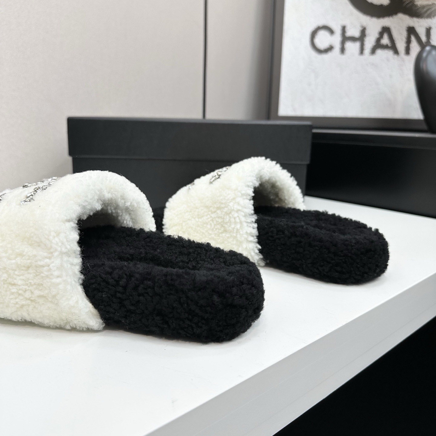 Pair of black and white fluffy shearling slides with a crystal-embellished interlocking logo sitting on a black box - Hình 7