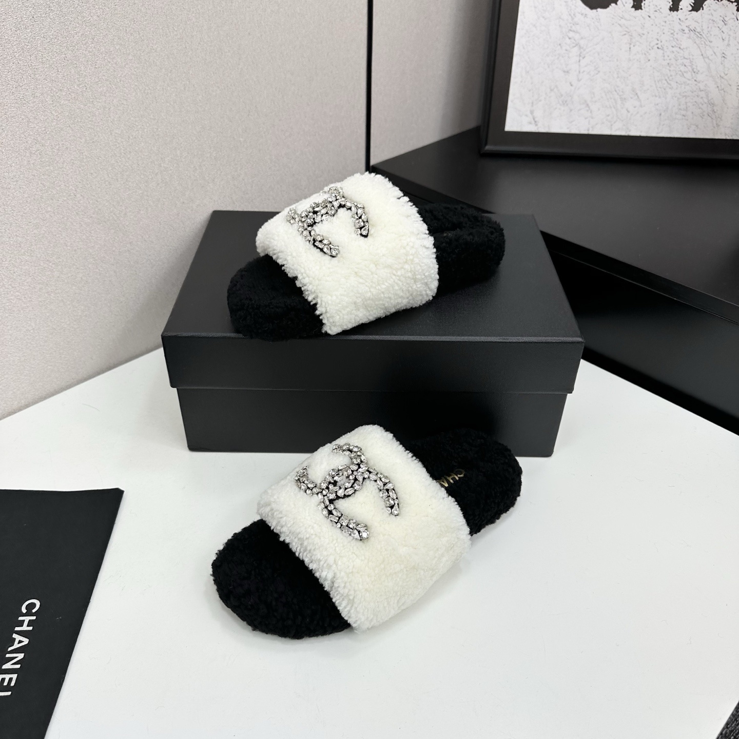 Pair of black and white fluffy shearling slides with a crystal-embellished interlocking logo sitting on a black box - Hình 2