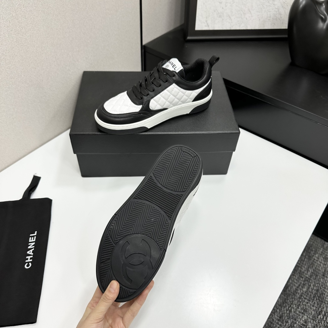 A pair of Chanel black and white quilted leather sneakers featuring the iconic CC logo on the side, displayed on a black box. - Hình 5