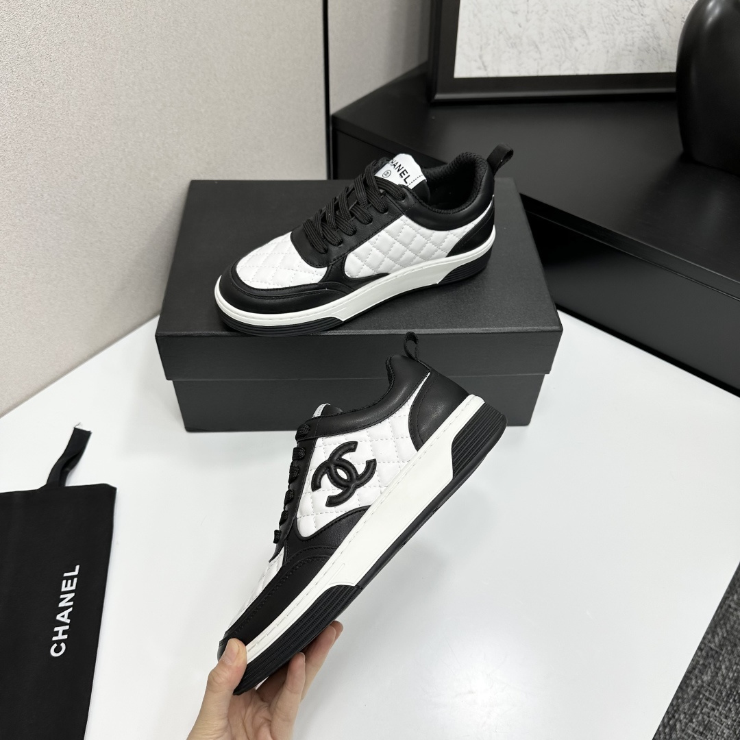 A pair of Chanel black and white quilted leather sneakers featuring the iconic CC logo on the side, displayed on a black box. - Hình 4
