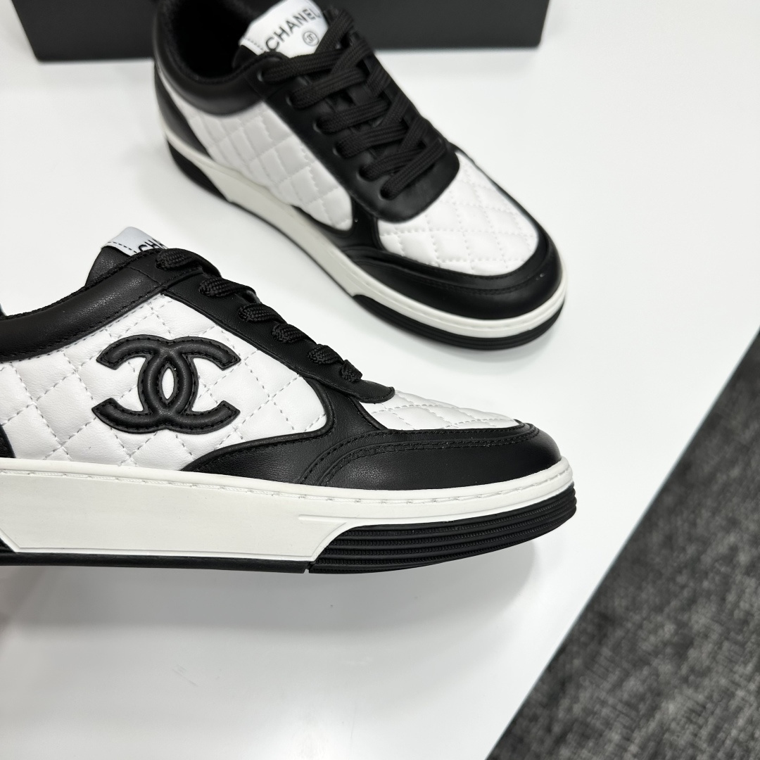 A pair of Chanel black and white quilted leather sneakers featuring the iconic CC logo on the side, displayed on a black box. - Hình 2