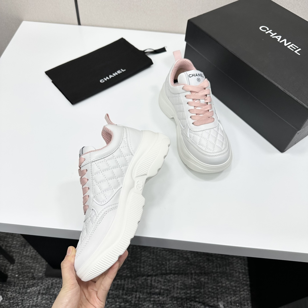 A pair of luxury Chanel white quilted platform sneakers with pink laces and pink interior lining displayed on a black box. - Hình 2