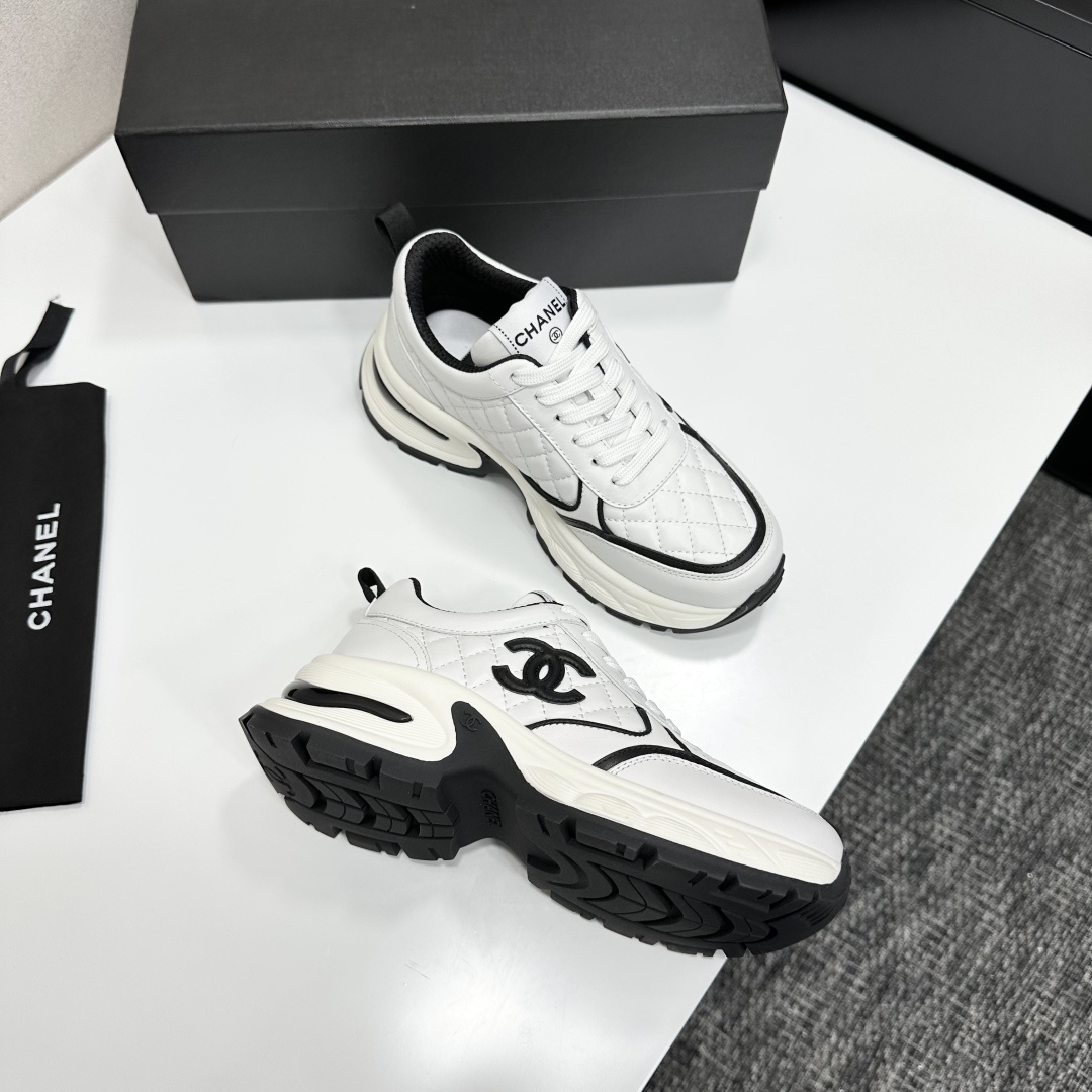 A pair of luxury Chanel white quilted leather sneakers with black CC logo and chunky white soles displayed on a black box. - Hình 9