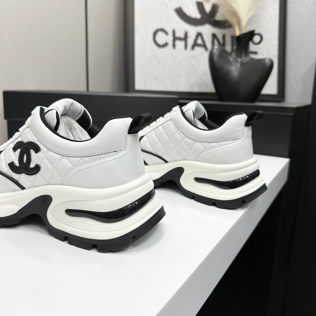 A pair of luxury Chanel white quilted leather sneakers with black CC logo and chunky white soles displayed on a black box. - Hình 8
