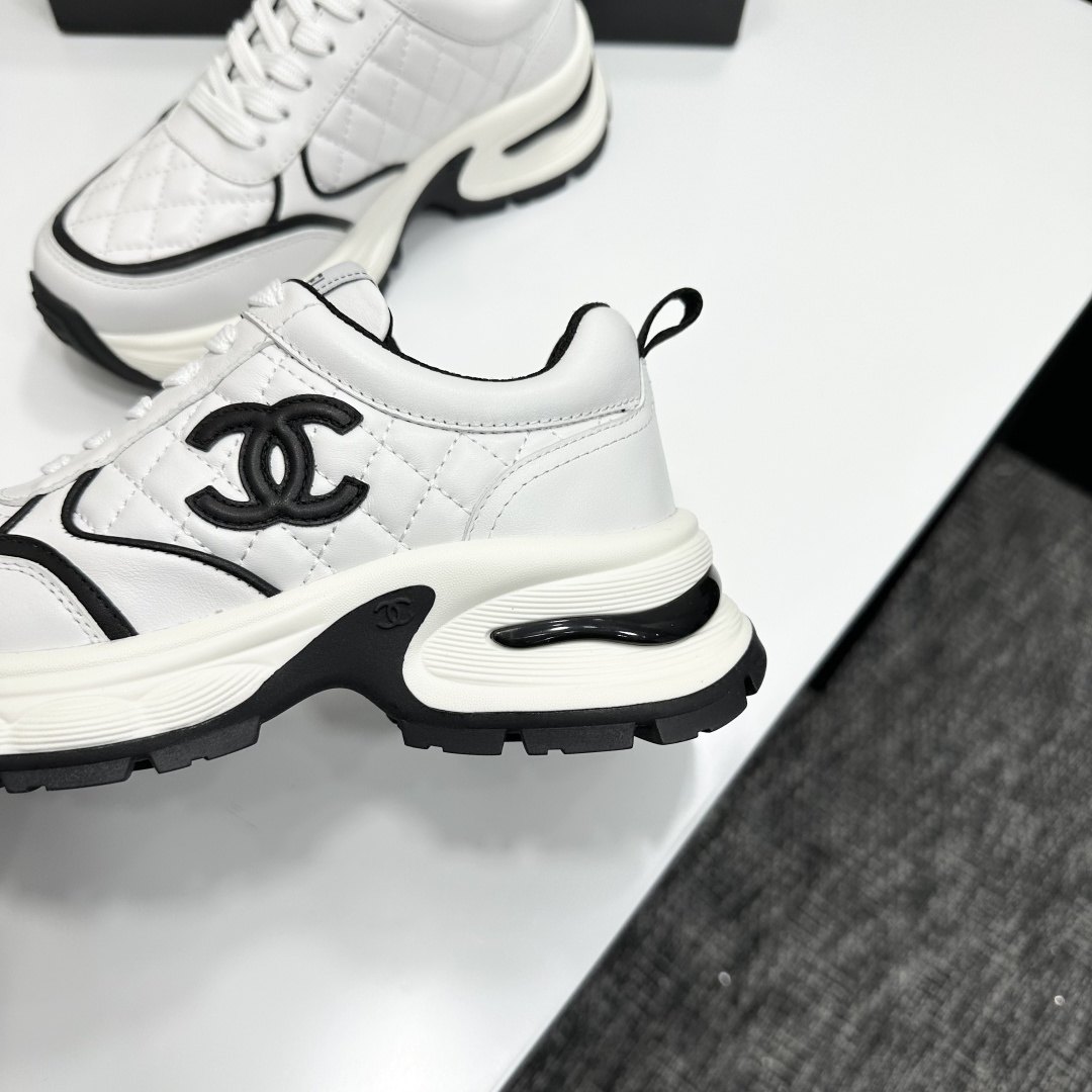 A pair of luxury Chanel white quilted leather sneakers with black CC logo and chunky white soles displayed on a black box. - Hình 7