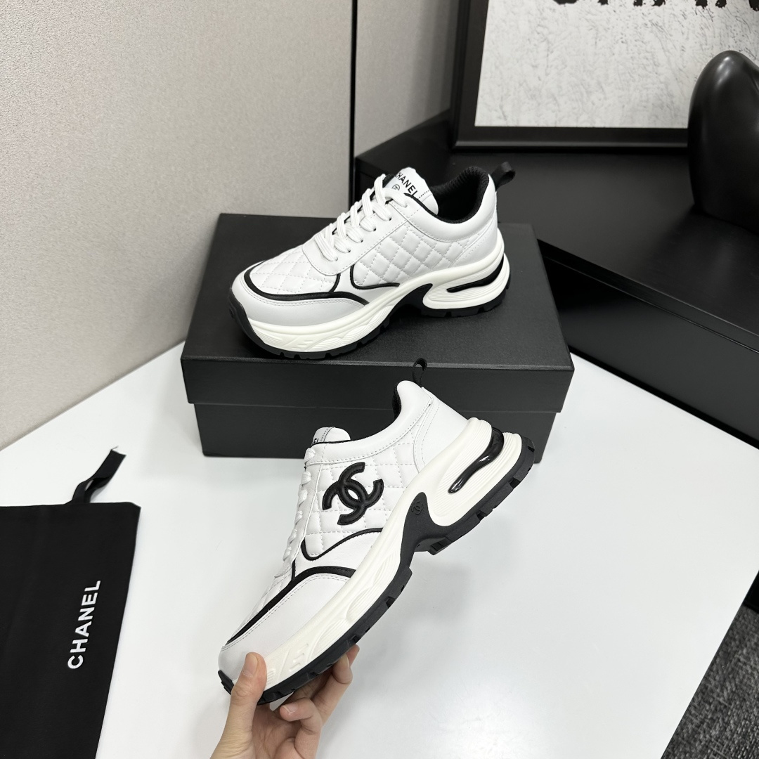 A pair of luxury Chanel white quilted leather sneakers with black CC logo and chunky white soles displayed on a black box. - Hình 4