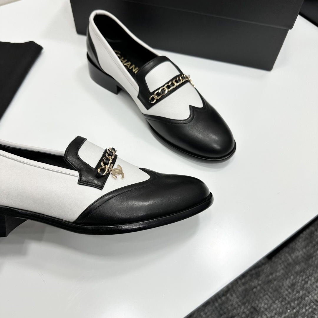 Pair of Chanel black and white two-tone leather loafers with gold chain detail on a black box - Hình 2
