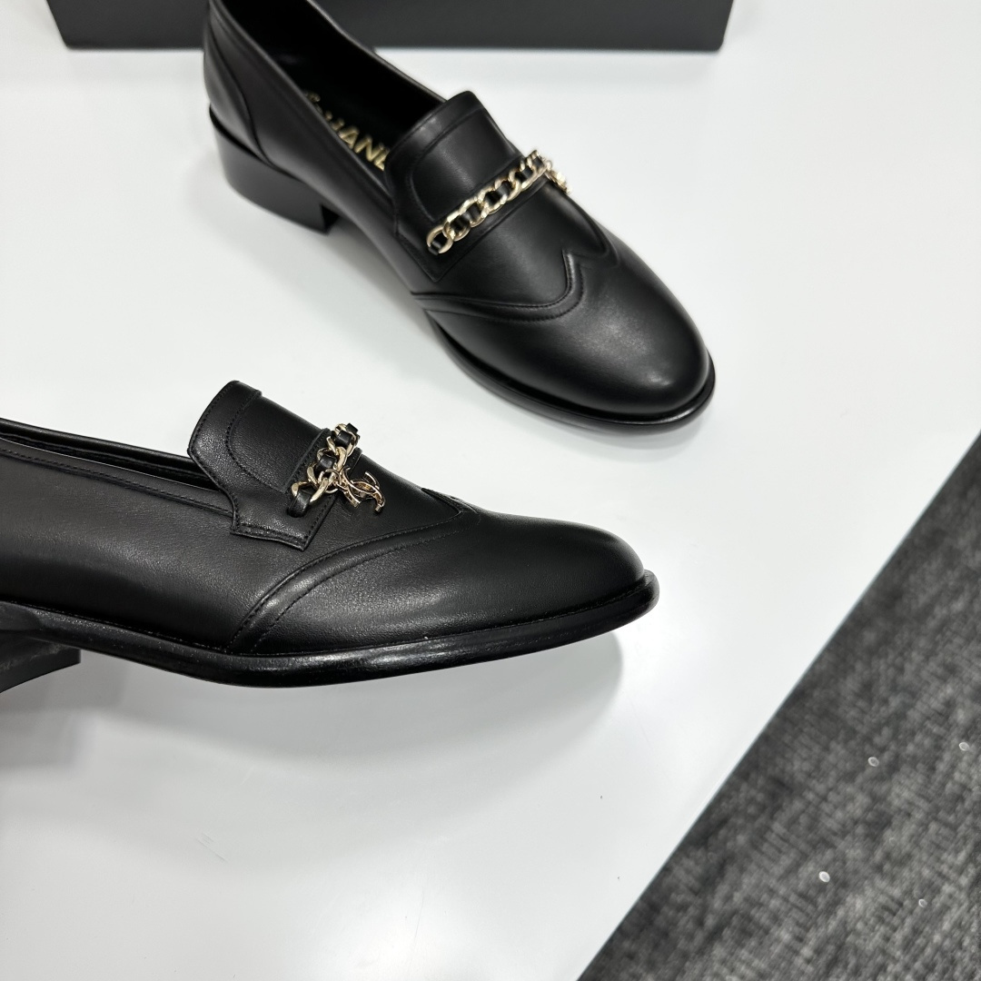 Classic black leather loafers with a gold chain and interlocking CC logo detail resting on a black shoebox. - Hình 9