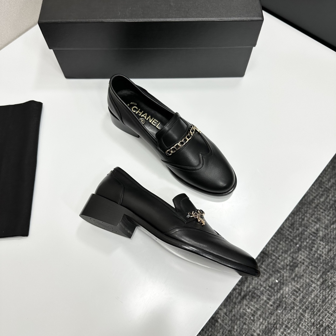 Classic black leather loafers with a gold chain and interlocking CC logo detail resting on a black shoebox. - Hình 8