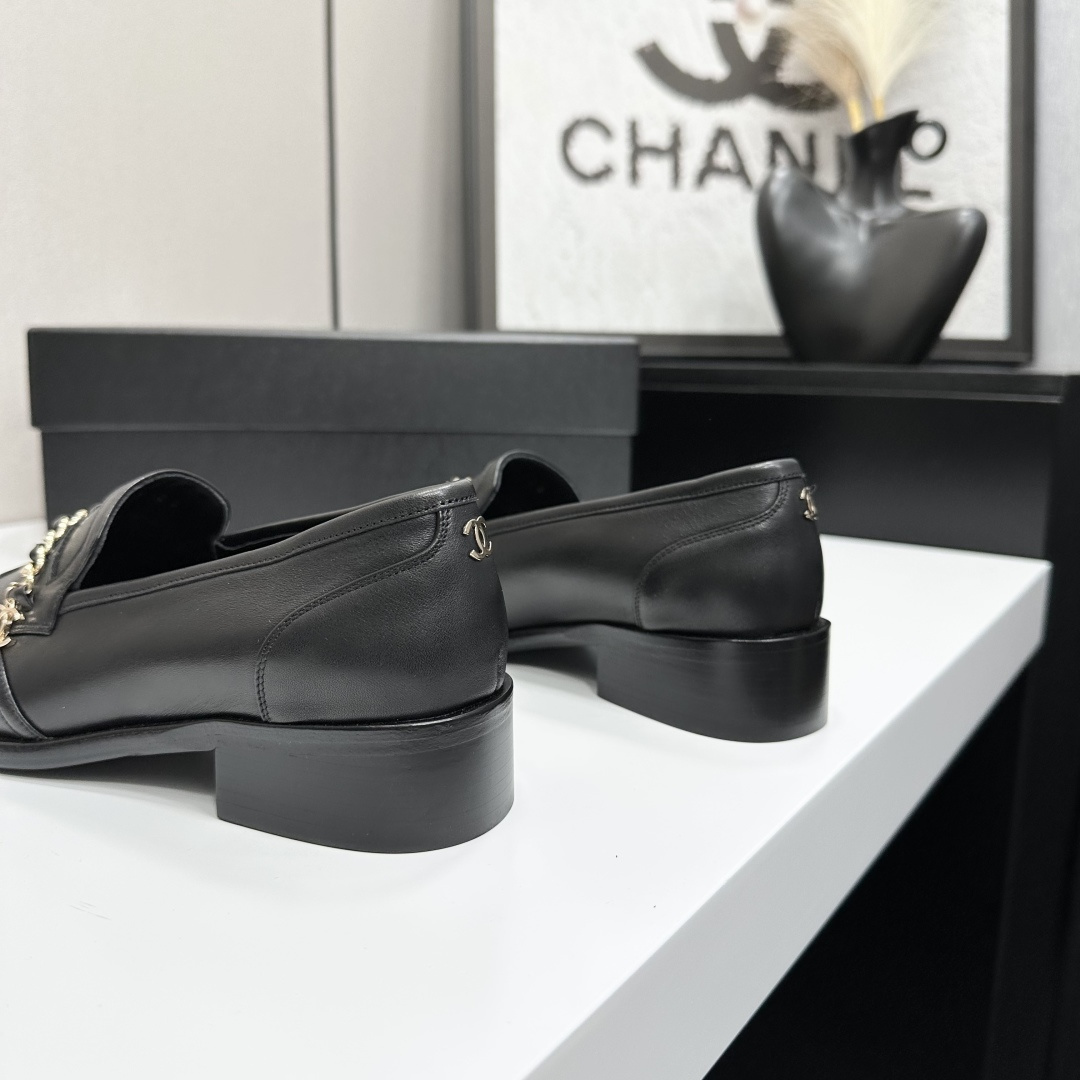 Classic black leather loafers with a gold chain and interlocking CC logo detail resting on a black shoebox. - Hình 7