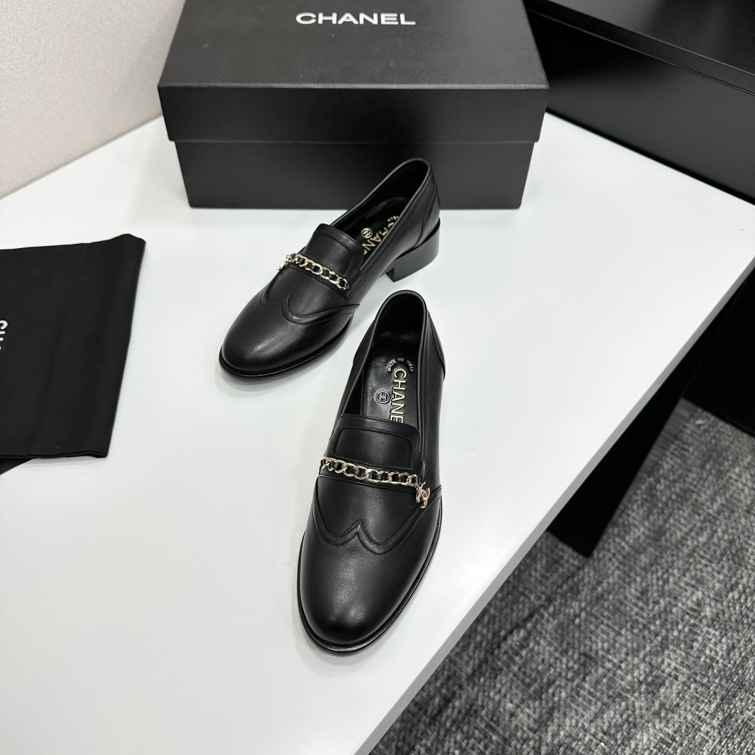 Classic black leather loafers with a gold chain and interlocking CC logo detail resting on a black shoebox. - Hình 5