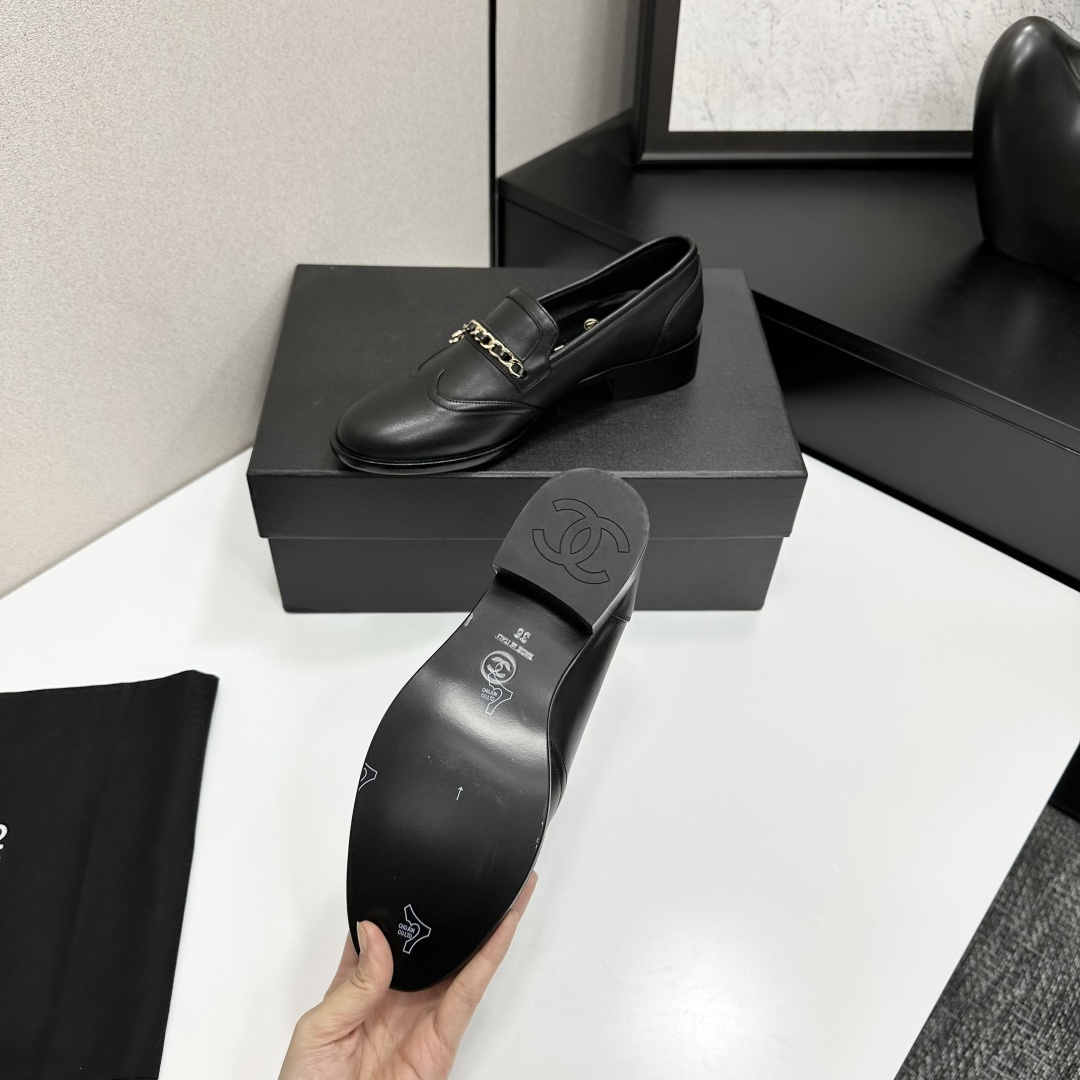 Classic black leather loafers with a gold chain and interlocking CC logo detail resting on a black shoebox. - Hình 4