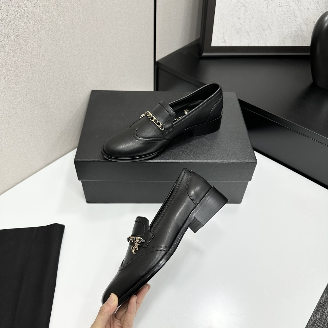 Classic black leather loafers with a gold chain and interlocking CC logo detail resting on a black shoebox. - Hình 3