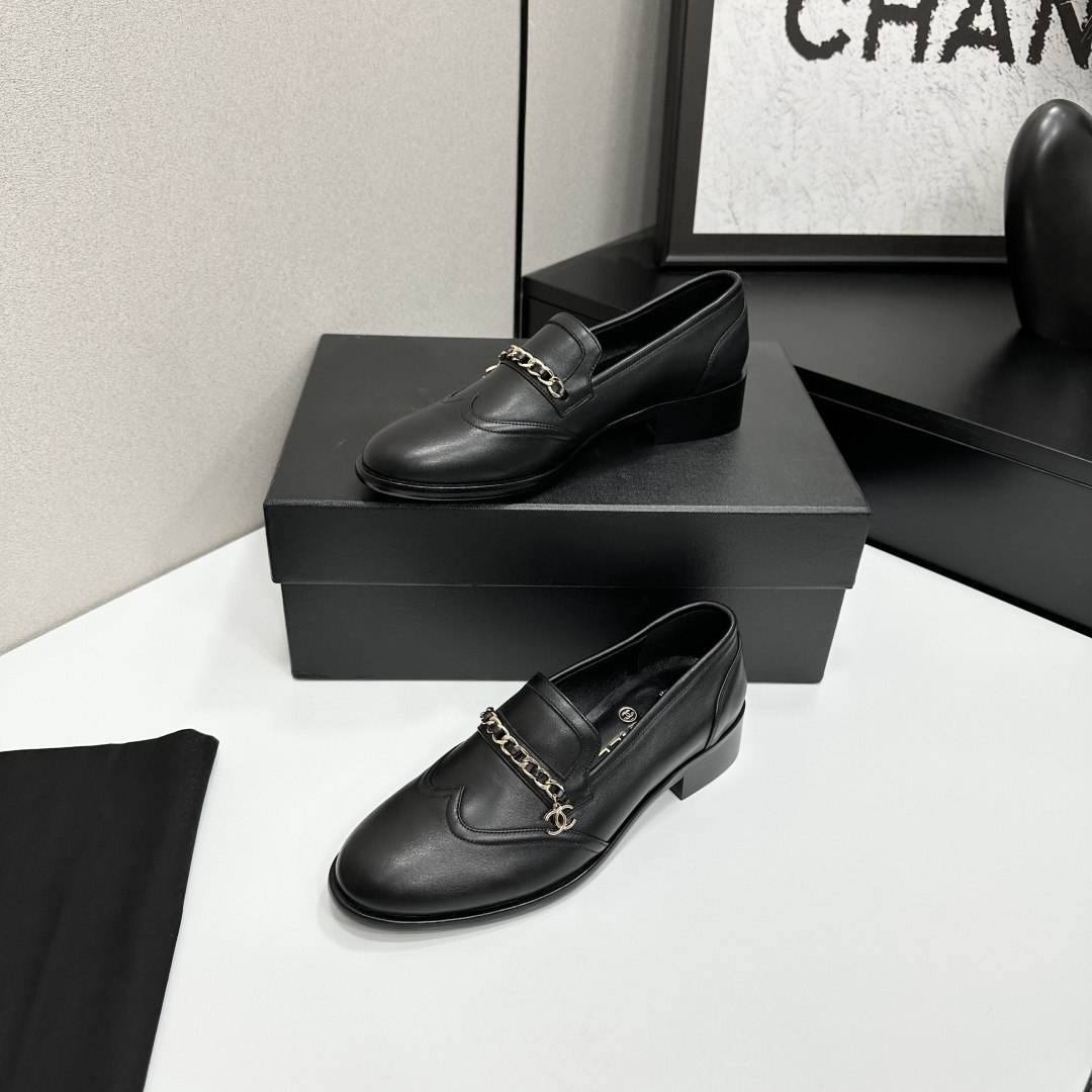 Classic black leather loafers with a gold chain and interlocking CC logo detail resting on a black shoebox. - Hình 2