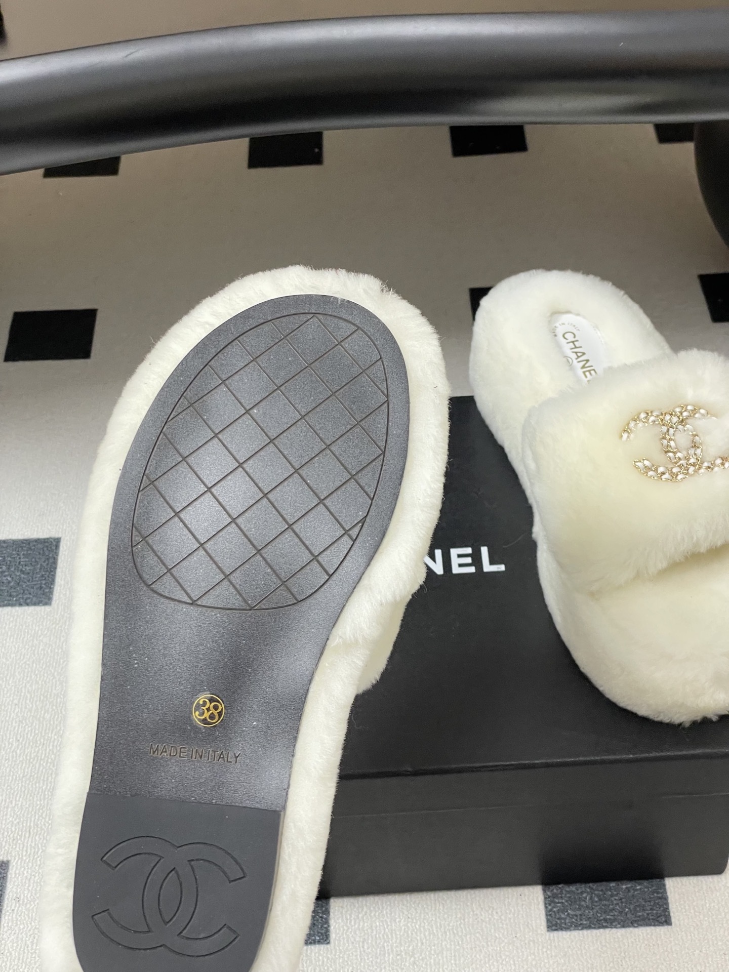 Pair of luxury Chanel white shearling fur slides with gold interlocking CC logo on a black surface. - Hình 8