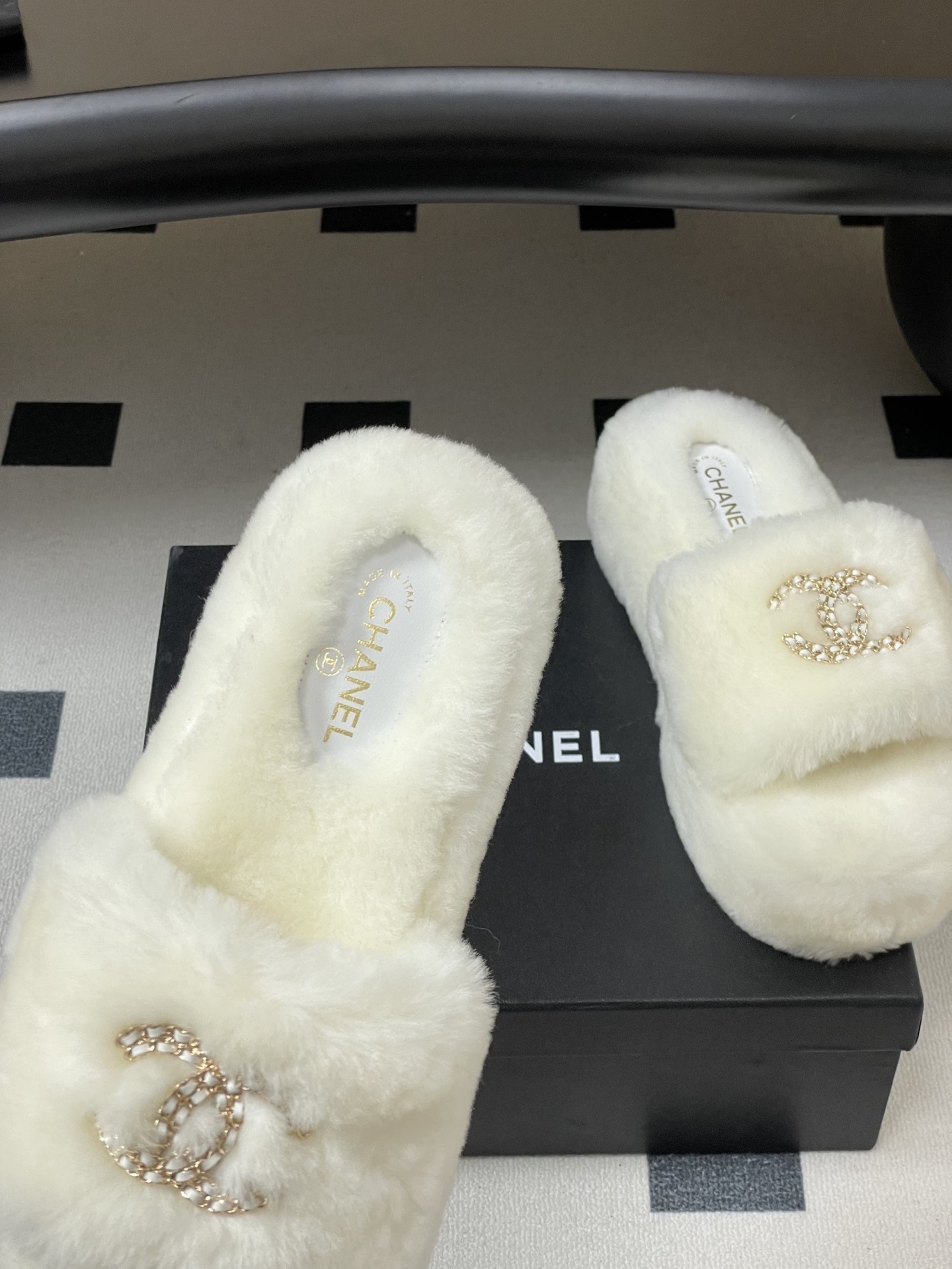 Pair of luxury Chanel white shearling fur slides with gold interlocking CC logo on a black surface. - Hình 7