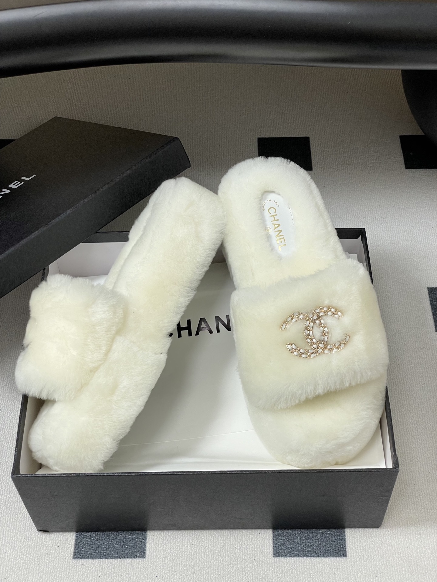 Pair of luxury Chanel white shearling fur slides with gold interlocking CC logo on a black surface. - Hình 6