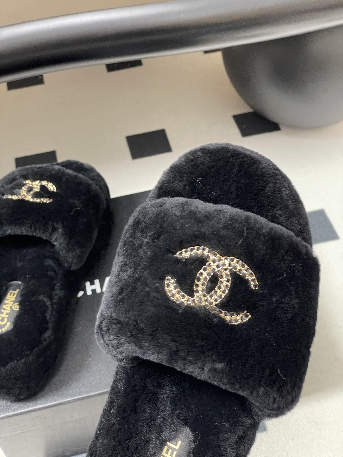 Pair of black Chanel shearling platform slides with gold chain interlocking CC logo on a black table. - Hình 9